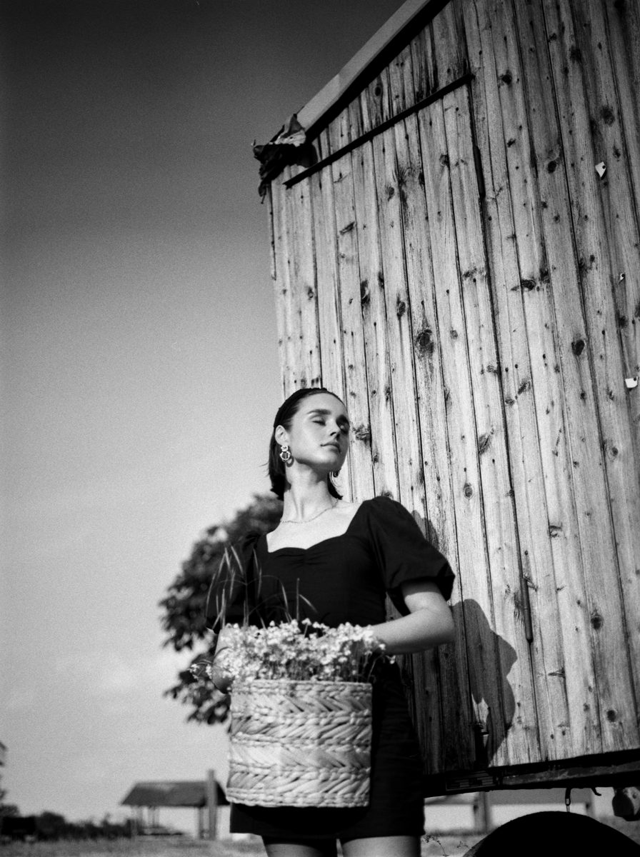 Michèl Passin. Black and white portrait of a woman stood up holding basket full of flowers.