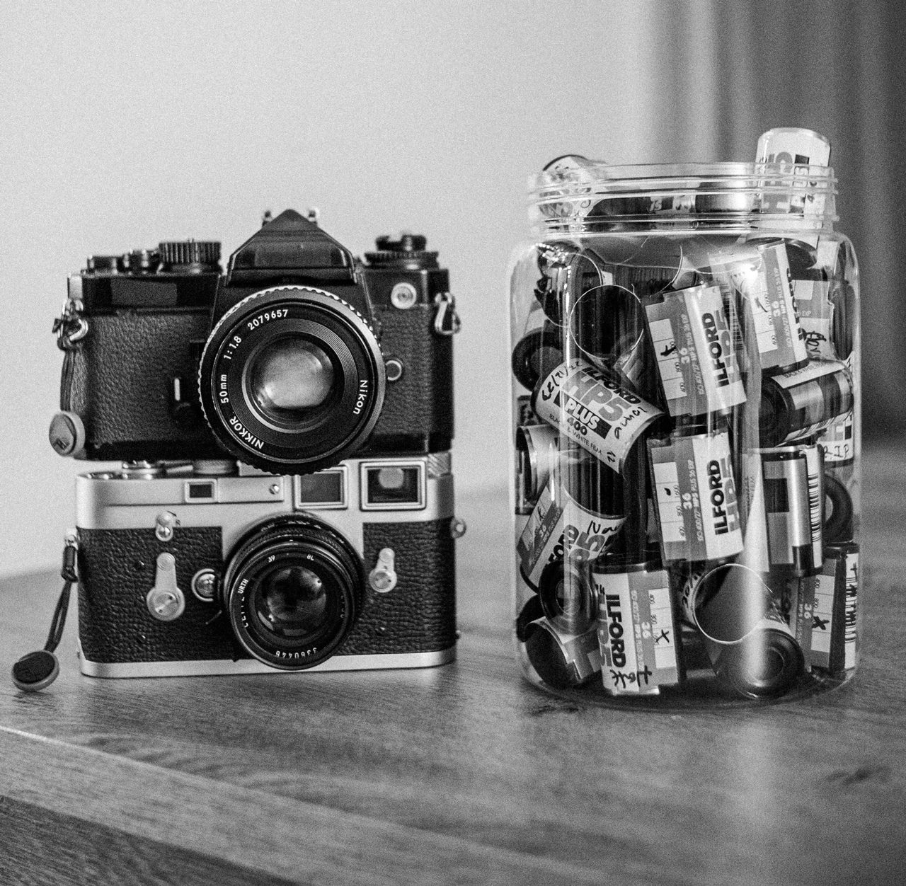 Álvaro Alberto. Black and white image of two cameras stacked next to a jar full of cassettes.