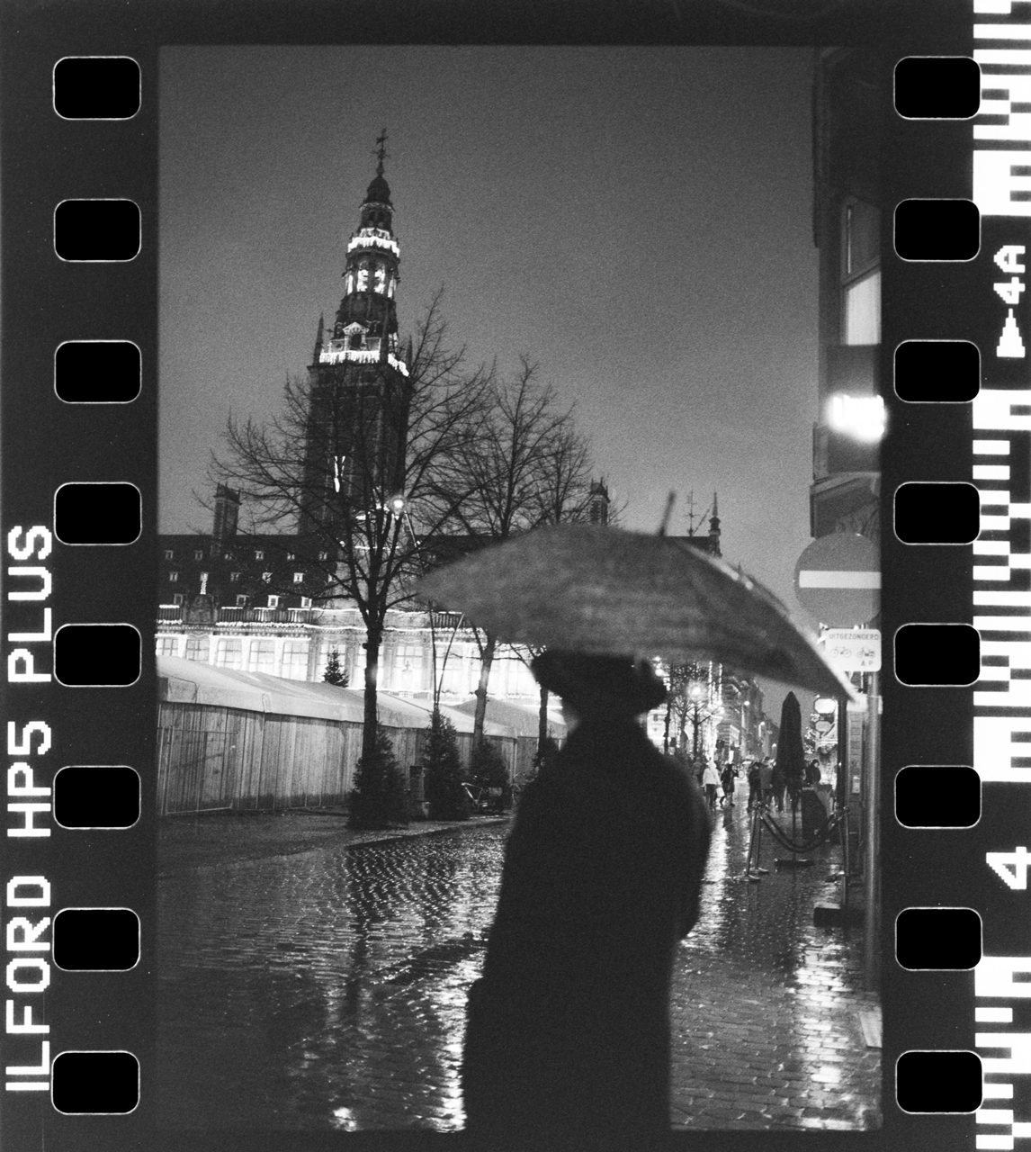 Álvaro Alberto. Black and white night time image of a person holding an umbrella in the street.