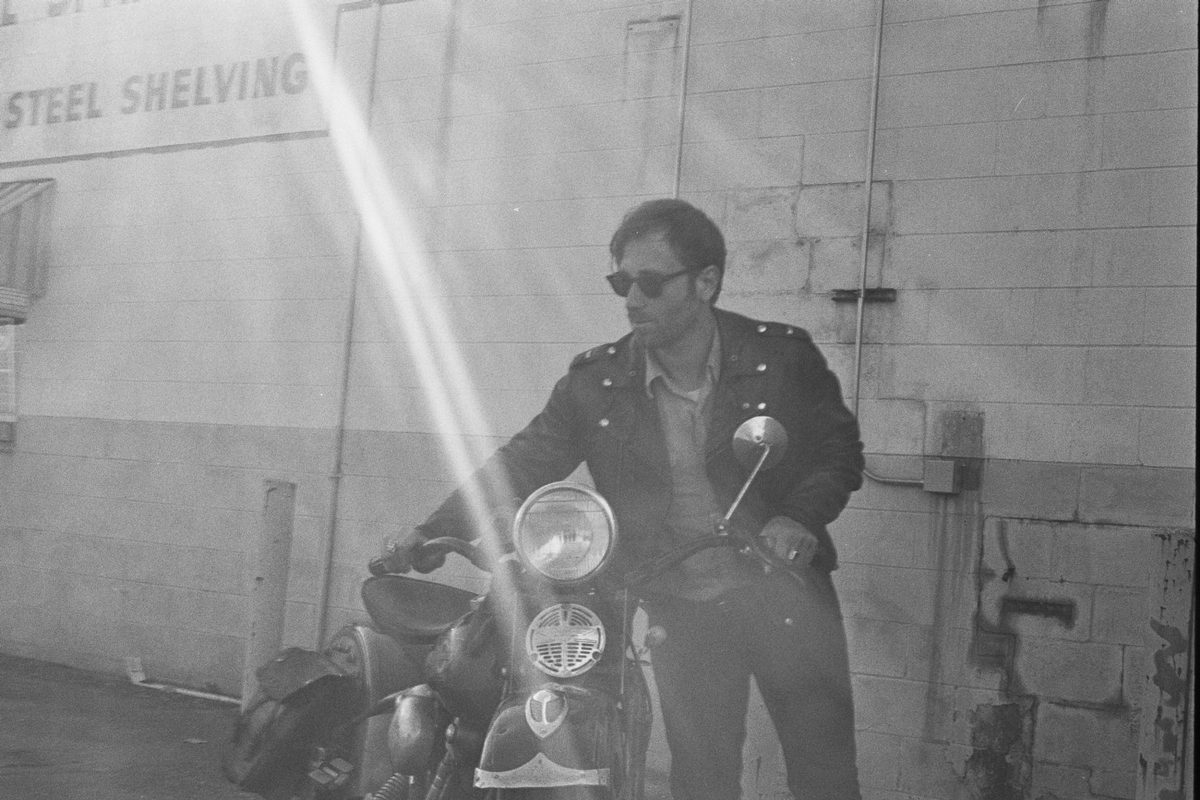 Larry Niehues. Black and white shot of a man holding his motorbike.