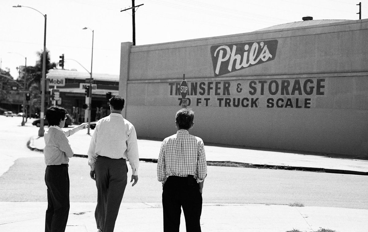 Larry Niehues. Black and white shot of three men walking cross the road.