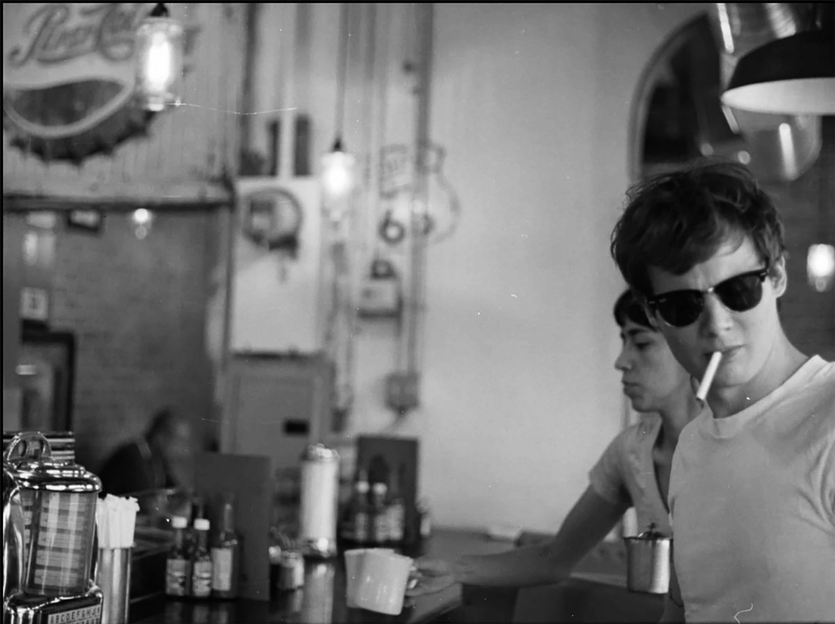 Larry Niehues. Black and white shot of a man smoking a cigarette in a cafe.