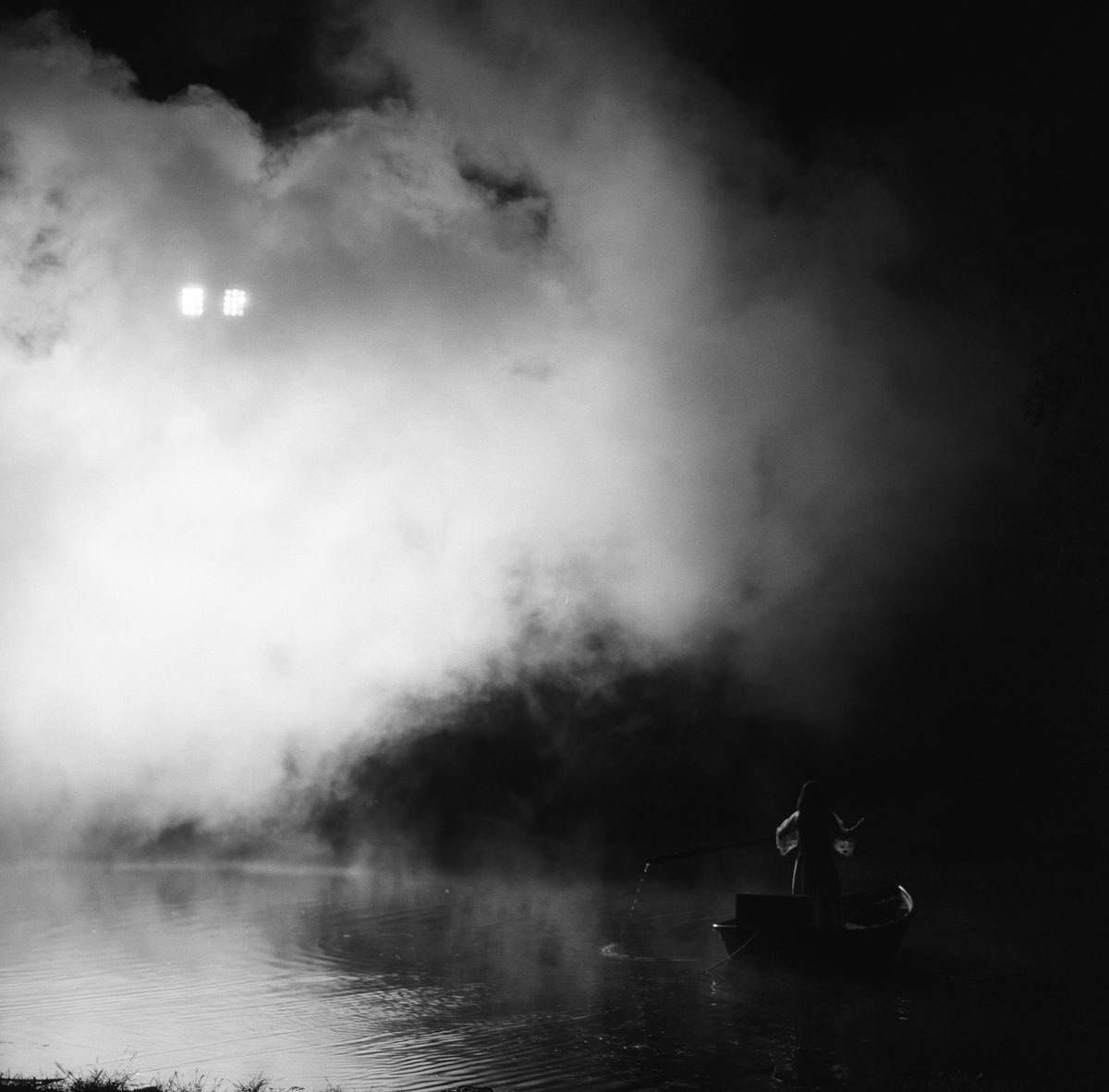 Hannah Baker. Black and white image of a woman on stood on a boat going down a river with misty clouds.