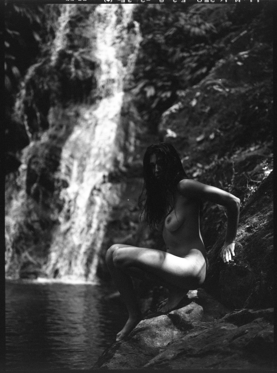 Clarissa Sofia. Black and white image of a naked woman in front of a waterfall.