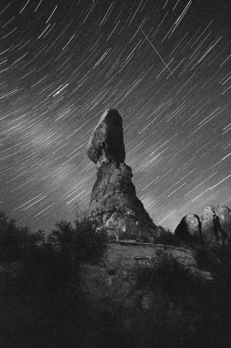 How I got this picture Ross McDaniel. Black and white long exposure image of stars at night with a large rock in the centre.