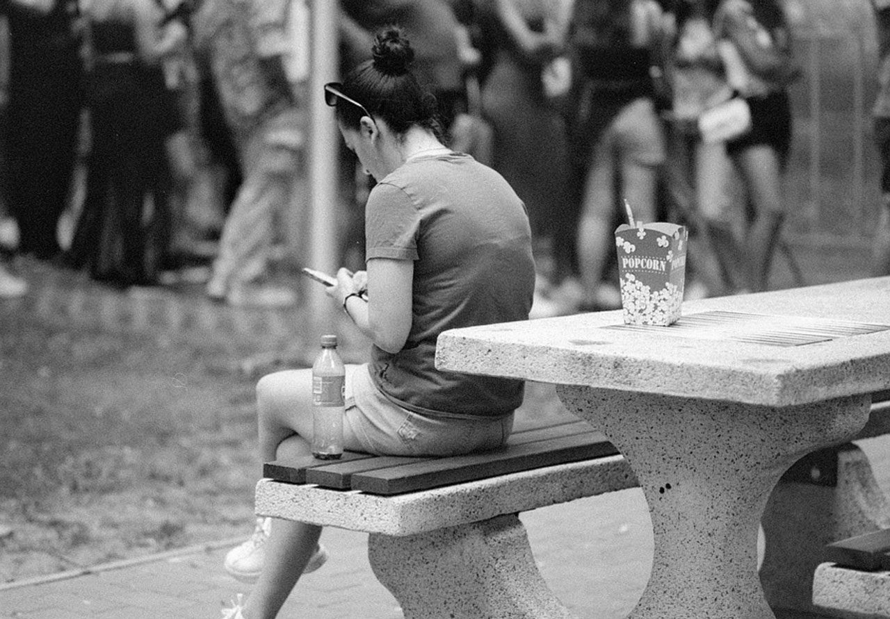 Julian Tanase. Black and white shot of a girl sat on a bench on her phone