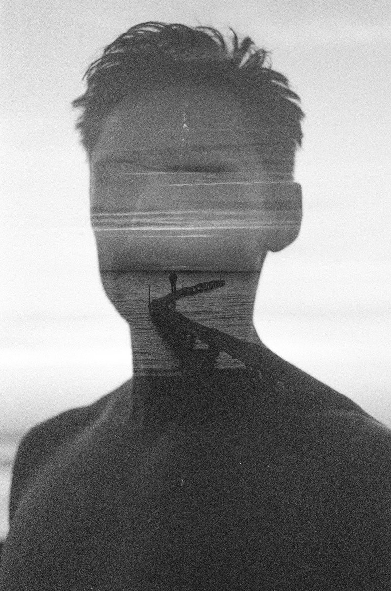 Euan Grimley. Black and white double exposure portrait with a pier and see going through the middle.