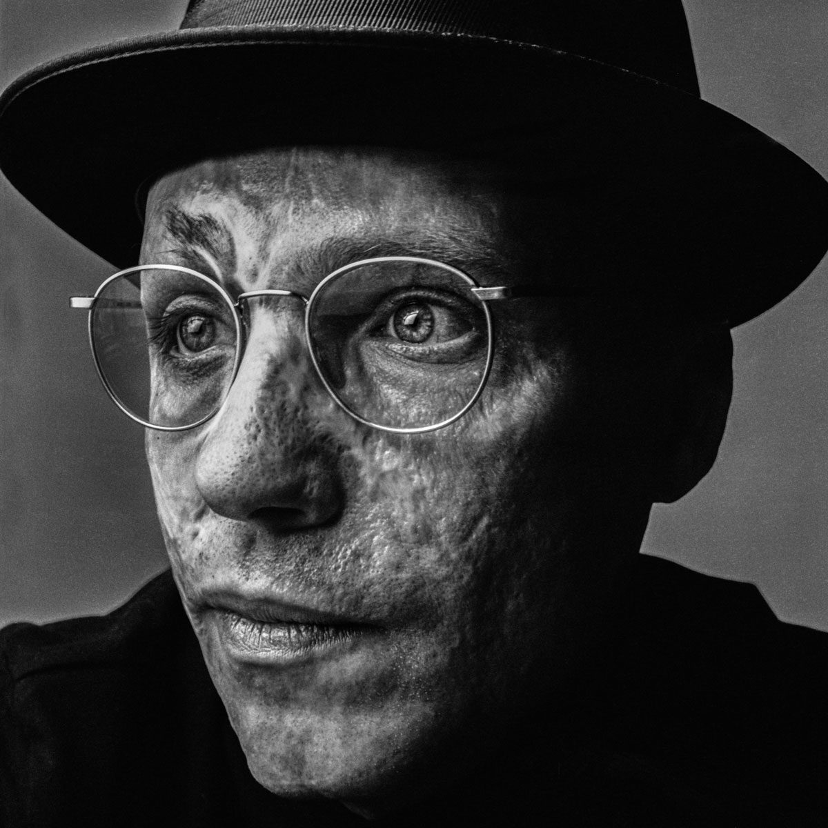 In Focus Jakob Stolz. Black and white portrait of a man with glasses and a hat on with his face slightly turned.