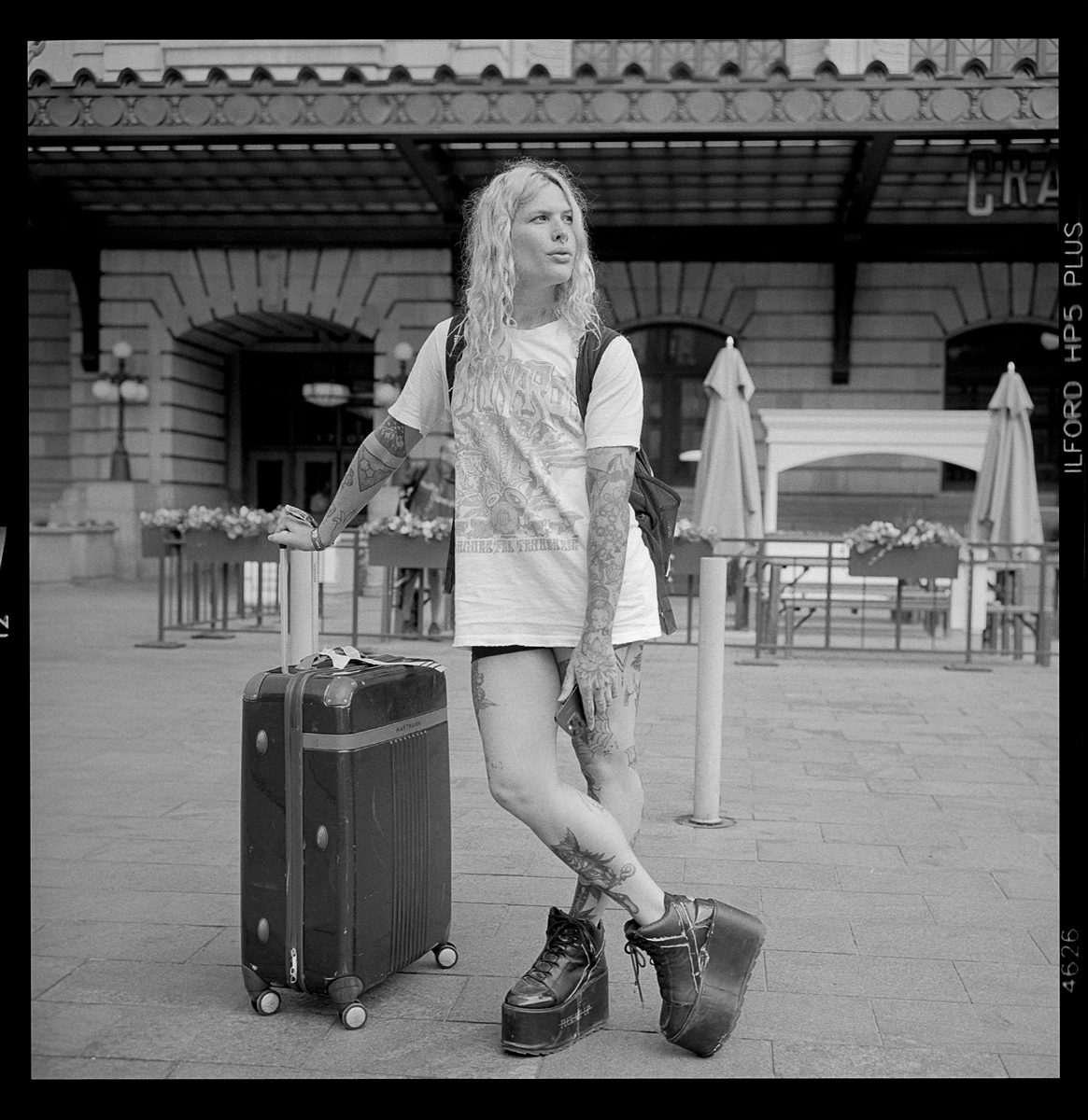 Kenneth Wadja. Black and white portrait of a blonde woman with her suitcase at the train station.