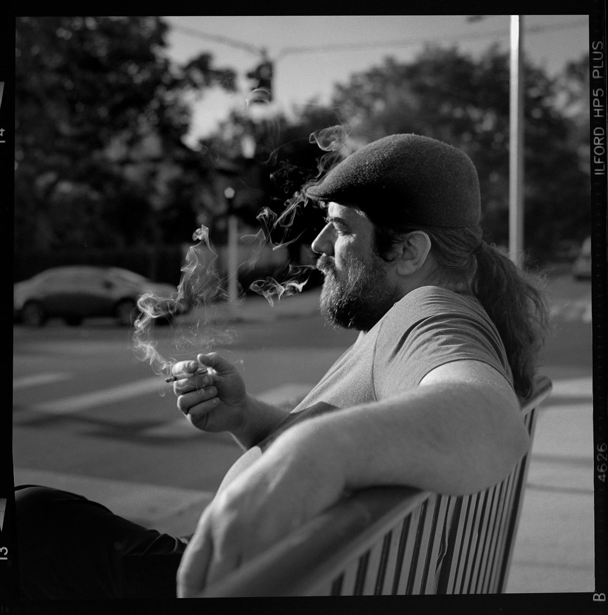 Kenneth Wadja. Black and white portrait of a man smoking a cigarette on a bench.